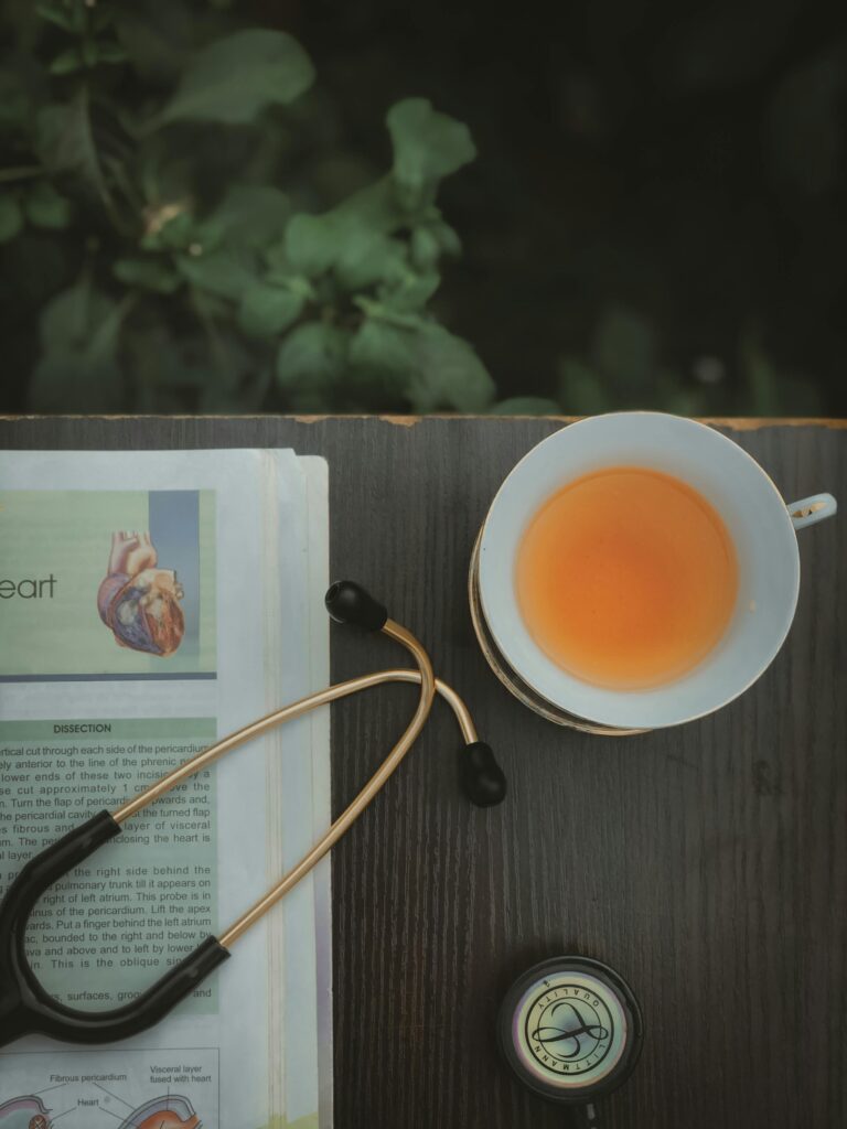 Flat lay of tea cup, stethoscope, and heart health book on wooden surface.